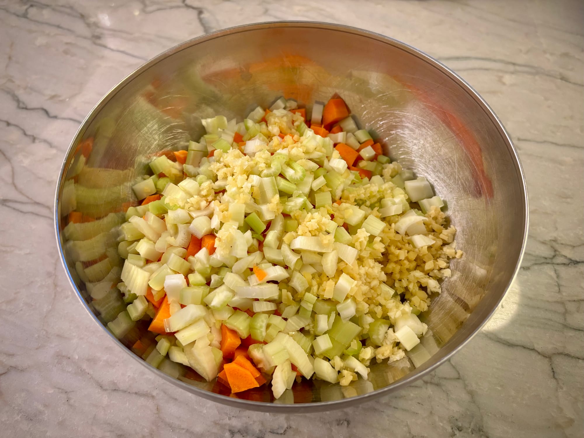 Chopped carrots, onions, celery, garlic and ginger, in a bowl.