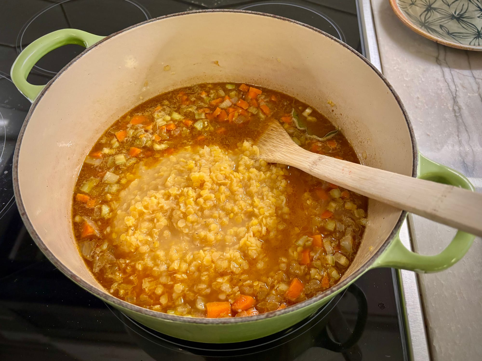A pot with broth, vegetables and red lentils.